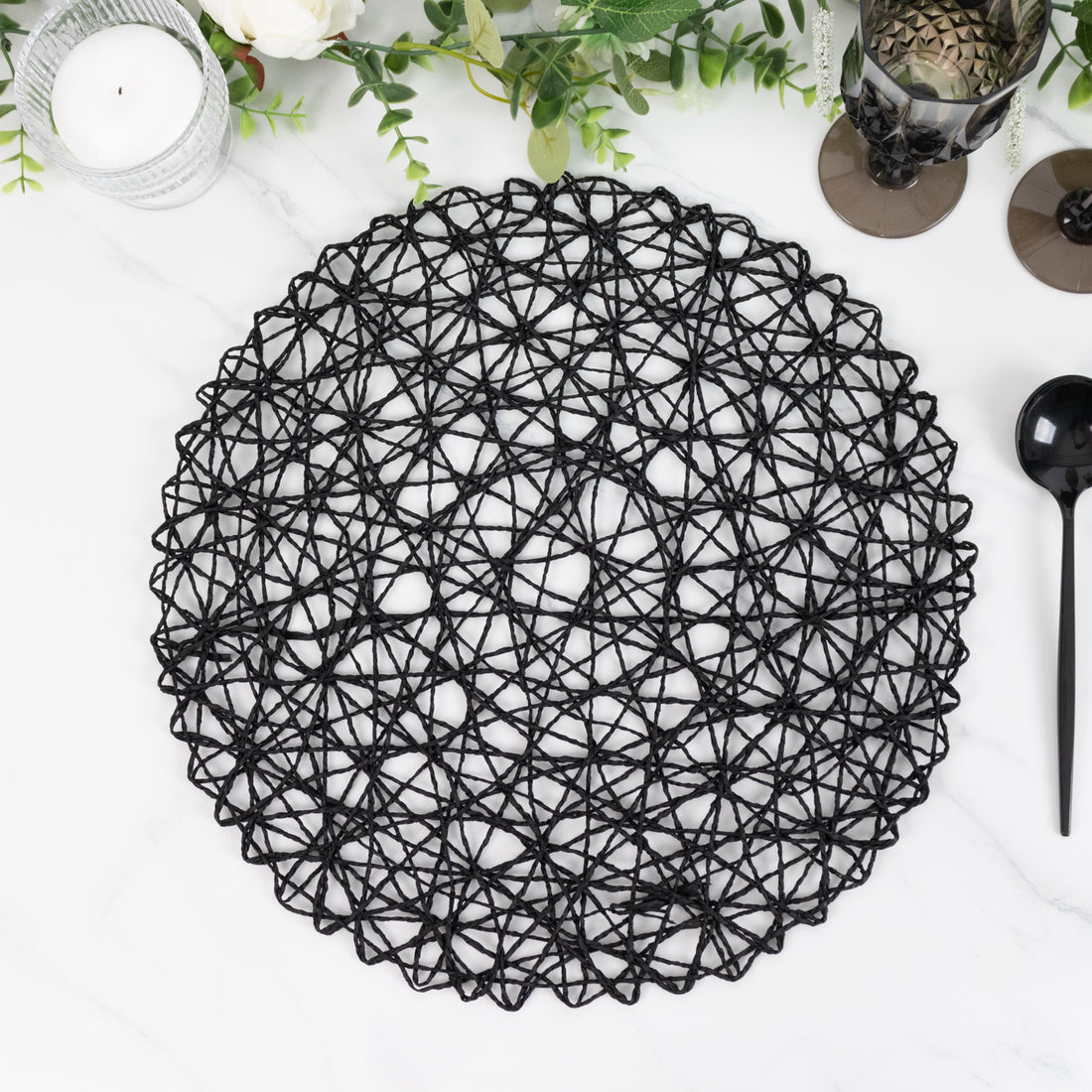 Black decorative placemat with intricate woven design on a marble surface.