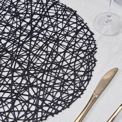 Black decorative placemat on a dining table with cutlery.