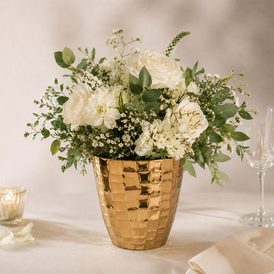 Elegant white floral arrangement in a gold textured vase on a table