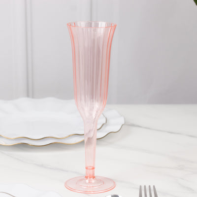 Pink ribbed champagne flute on a marble table with elegant plates in the background.