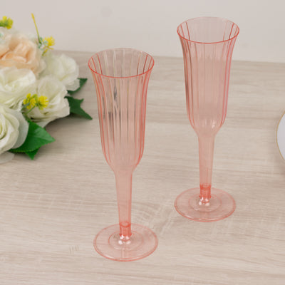 Pink plastic champagne flutes on a wooden surface.