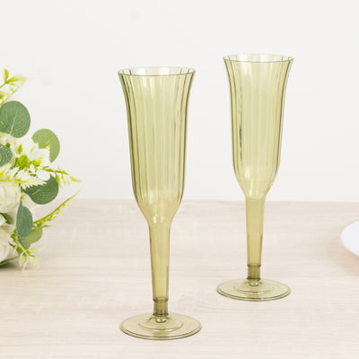 Two elegant green champagne flutes on a light wooden surface.