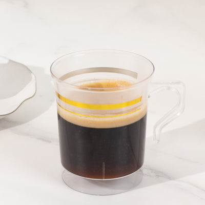Transparent coffee mug with gold stripes, filled with dark coffee.