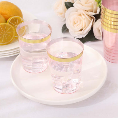 Pink plastic cups with gold rims on a white plate with lemons and flowers.