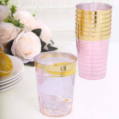 Pink plastic cups with gold rims, stacked and one filled with water.