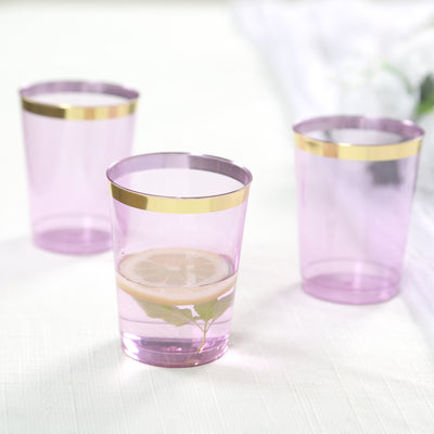 Set of three pink plastic cups with gold rims, one filled with water and lemon.