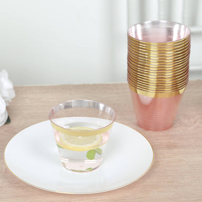 Clear plastic cups with gold rims on a table with a drink and lemon slice.