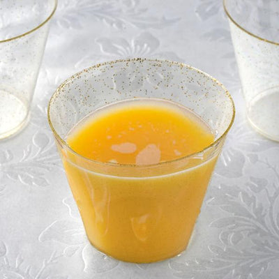 Gold-rimmed glass filled with orange juice on a textured surface.