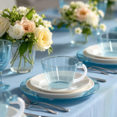 Blue transparent cup with white plates and floral centerpiece on a table setting.