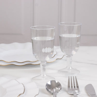 Clear plastic glasses with water on a marble table with elegant plates and silverware.