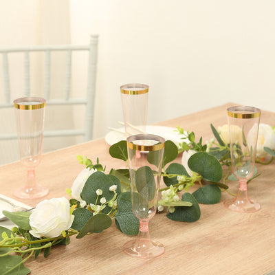Elegant pink and gold champagne flutes arranged on a table with greenery.