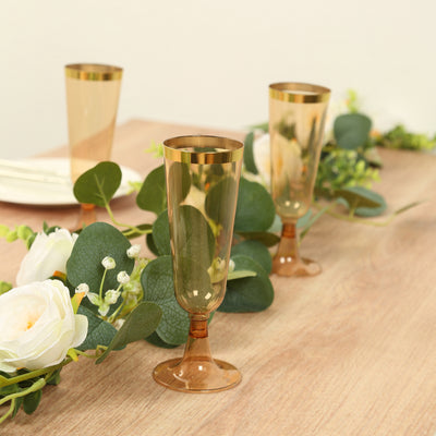 Gold rimmed champagne flutes on a table with greenery and flowers.