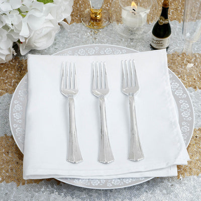 Three elegant silver forks arranged on a white napkin atop a decorative plate.