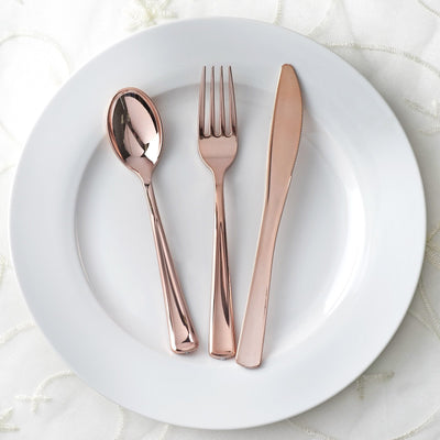 Rose gold cutlery set on a white plate, including a spoon, fork, and knife.