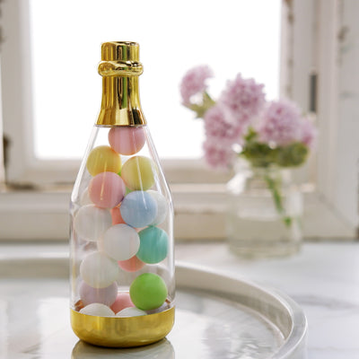 Colorful pastel balls in a clear bottle with a gold base on a marble tray.