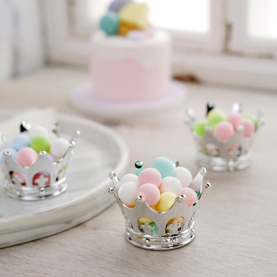 Colorful candy crowns on a table with a pastel cake in the background.