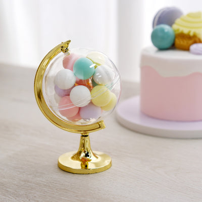 Colorful candy globe on a golden stand with a cake in the background.