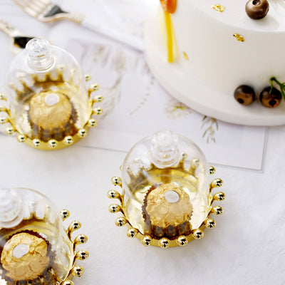 Decorative glass cloches with gold accents over chocolate treats and a cake.