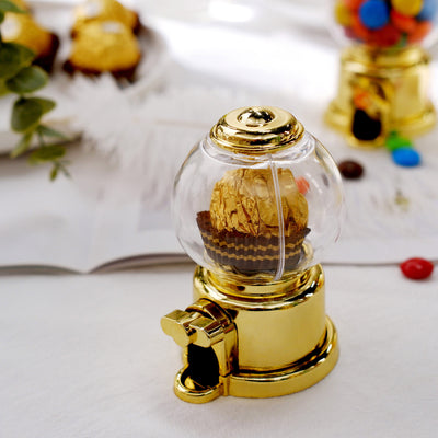 Gold gumball machine filled with chocolate candies on a table.