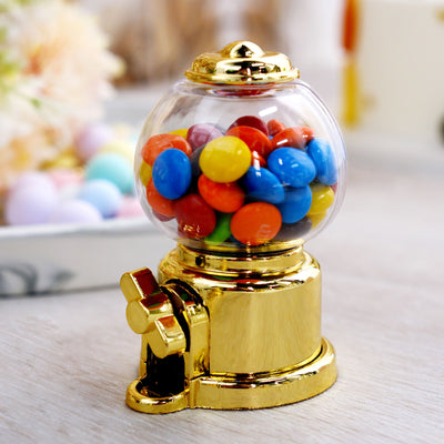Gold gumball machine filled with colorful candies on a table.