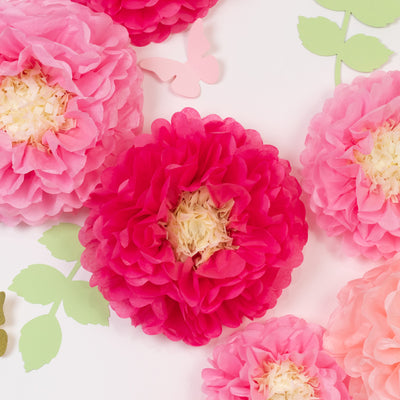 Colorful paper flowers in pink and red with green leaves and butterflies on a white background.