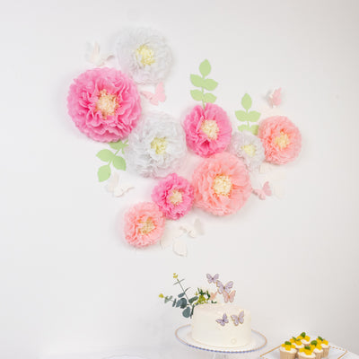 Colorful paper flowers decor with butterflies on a wall, cake on a table.