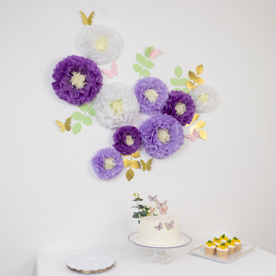 Decorative paper flowers and butterflies on a wall with a cake and cupcakes in front.