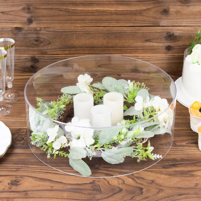 Clear glass dome with candles and floral arrangement on a wooden table.
