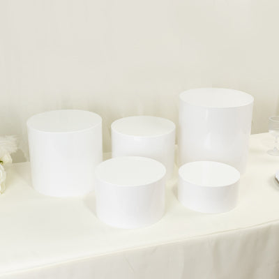White cylindrical display pedestals in various sizes on a neutral background.