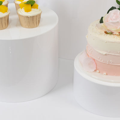 Assorted desserts including cupcakes and a decorated cake on white pedestals.