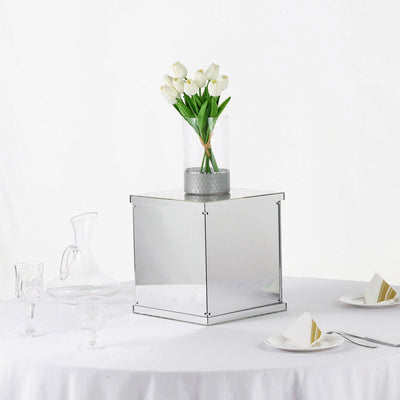 Mirrored square display cube with flowers and glassware on a table.