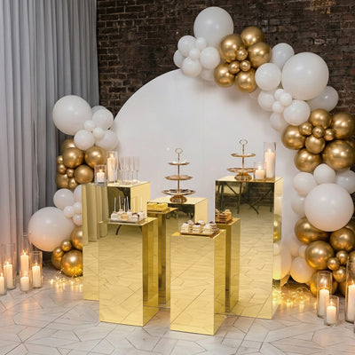 Gold display tables with desserts at a festive event, surrounded by balloons and candles.