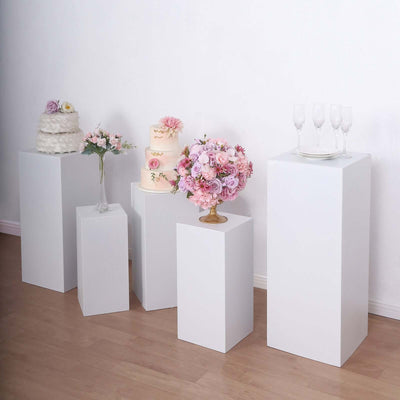 White pedestals displaying cakes and floral arrangements in a styled setting.