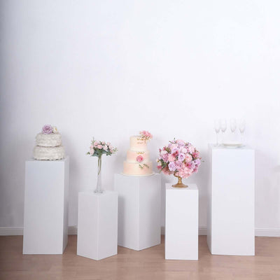Elegant display of cakes and floral arrangements on pedestals in a studio setting.