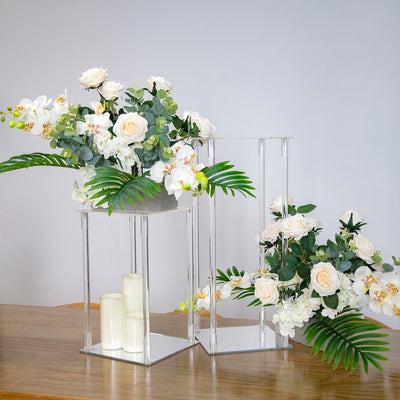 Acrylic flower vases with white roses and orchids on a wooden table.