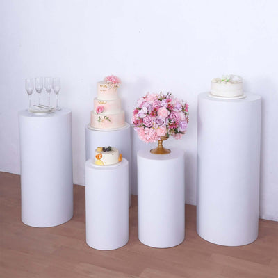 White pedestal display stands with cakes and flowers on a neutral background.