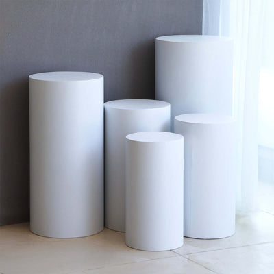 White cylindrical pedestals in varying heights on a minimalist background.