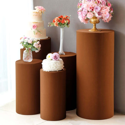 Brown pedestal tables with floral arrangements and a cake, styled for events.