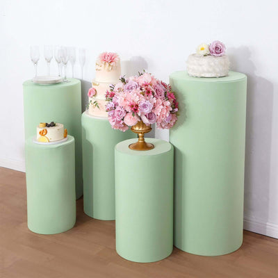 Display of five mint green pedestals with cakes and floral arrangements.