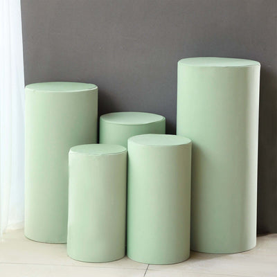 Set of five green cylindrical pedestals against a gray wall.