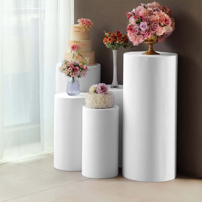 White pedestal stands decorated with flowers and cakes for events and celebrations.