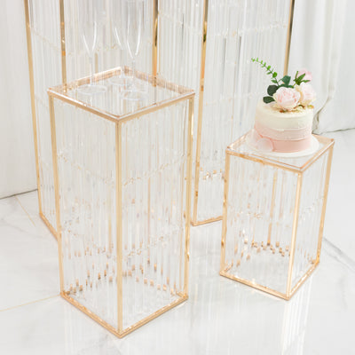 Elegant clear glass display pedestals with gold accents and a small cake on top.
