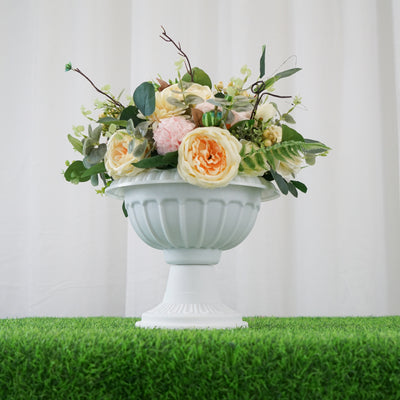White urn with mixed floral arrangement on green grass backdrop.
