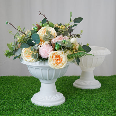White decorative urn with artificial flowers on green grass.
