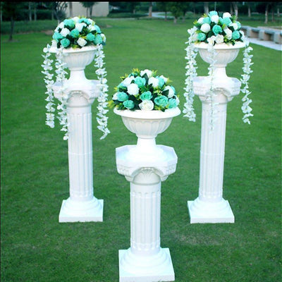 Three white columns with floral arrangements in a garden setting.