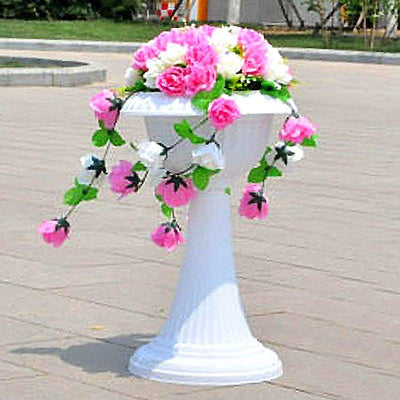 White pedestal vase with pink and white flowers cascading down.