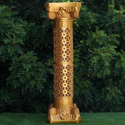 Decorative golden pedestal with intricate cutouts against greenery.
