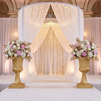 Elegant wedding ceremony backdrop with white drapes, fairy lights, and floral urns