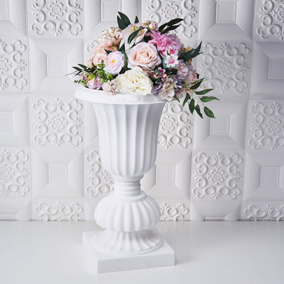 White decorative urn with a floral arrangement on a textured background.