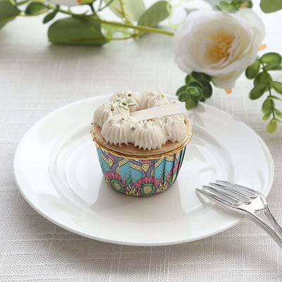 Colorful cupcake with frosting on a white plate, surrounded by greenery.